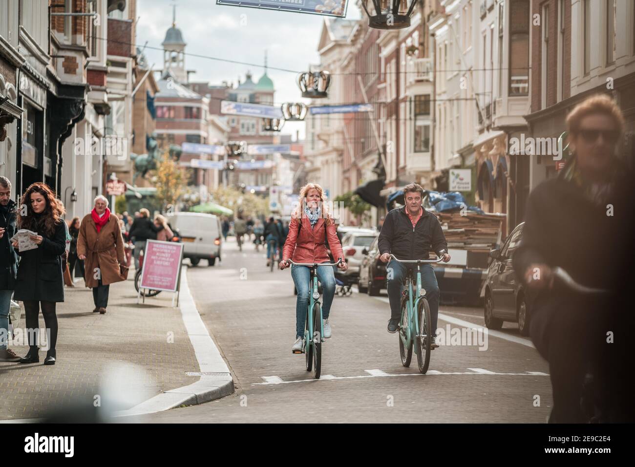 Uomo e donna coppia in bicicletta lungo la stretta strada dello shopping ad Amsterdam, Paesi Bassi pushbikes mescolando con pedoni in trafficata scena stradale Foto Stock