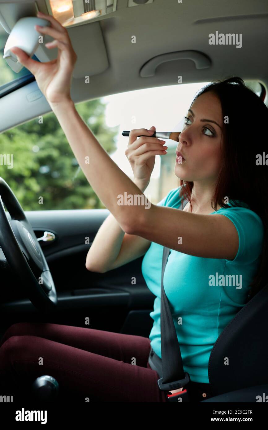 Donna mettendo su make up nella sua auto Foto Stock