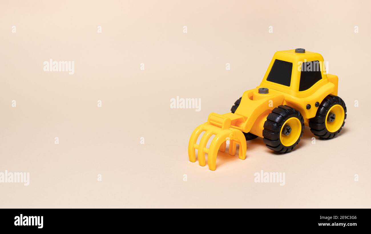 Trattore giocattolo giallo con ugello rastrello per caricare la foresta su uno sfondo beige per il negozio di giocattoli banner testo copyspace. Foto Stock
