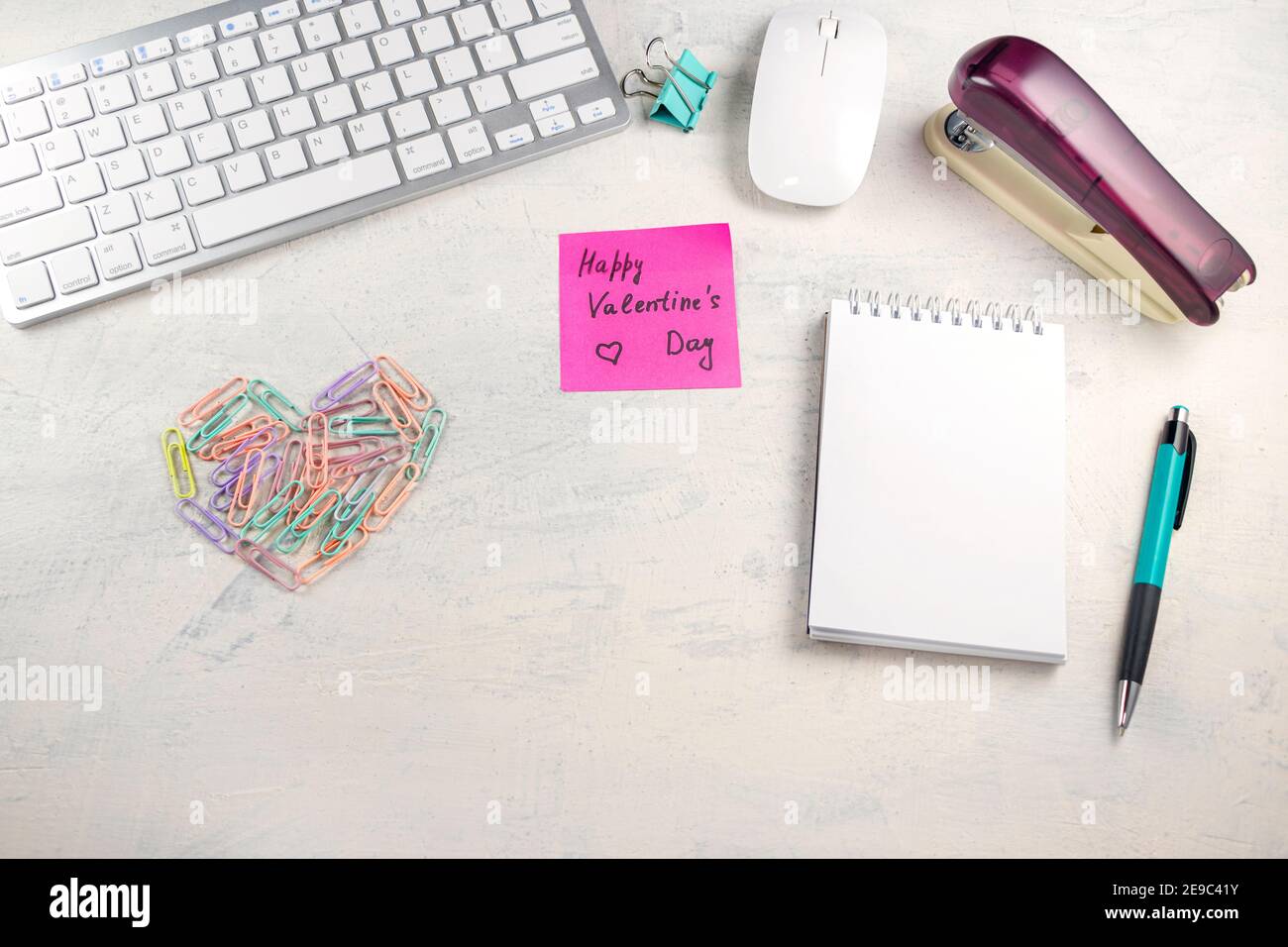 Parole buon San Valentino in una nota sul desktop con graffette colorate a forma di cuore e tastiera, penna, blocco note e pinzatrice al workpl Foto Stock