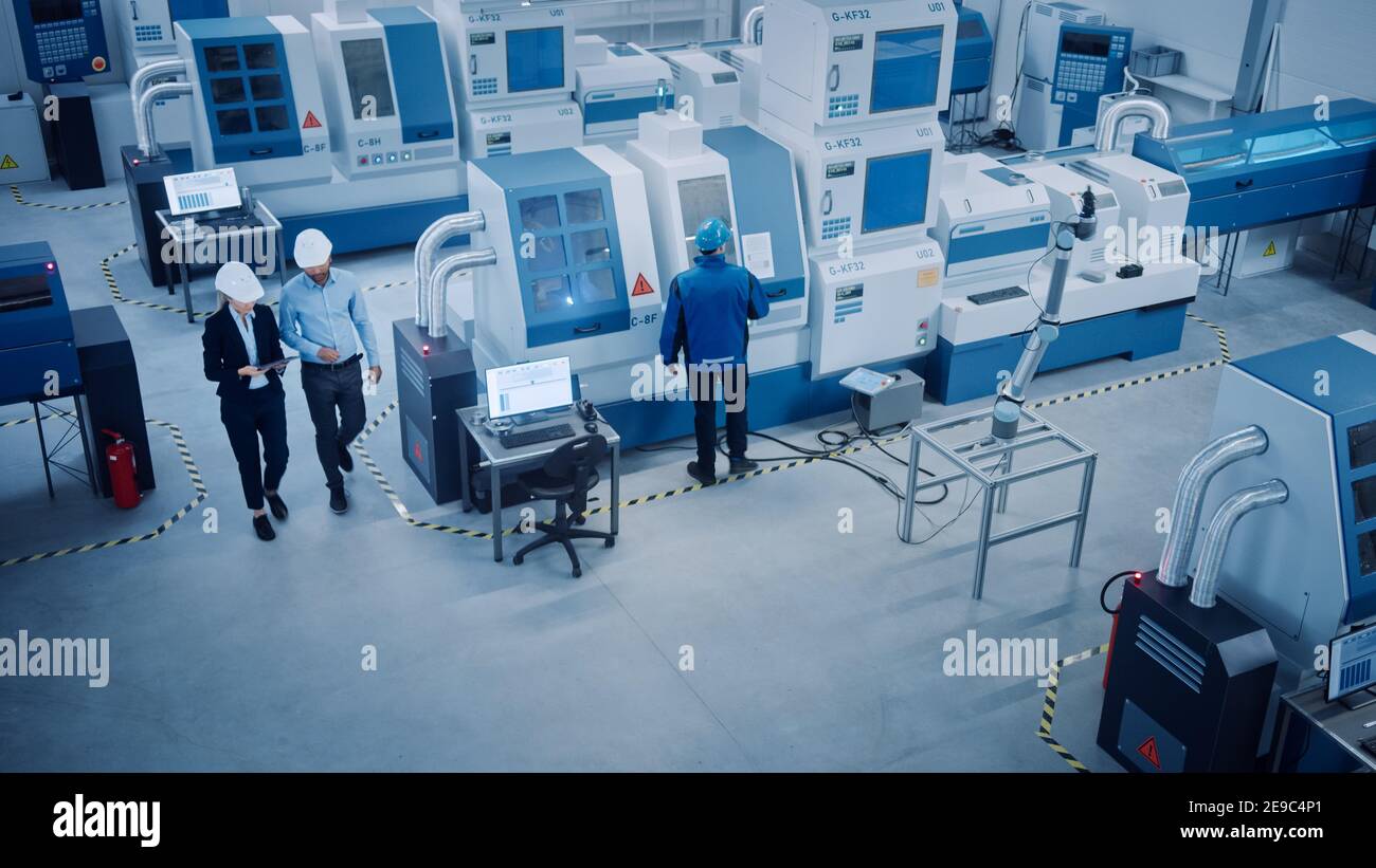 Industry Four Factory: Executive femminile e Chief Engineer Inspect Facility Workshop, esaminare il braccio del robot che lavora sulla linea di assemblaggio. CNC di fascia alta Foto Stock