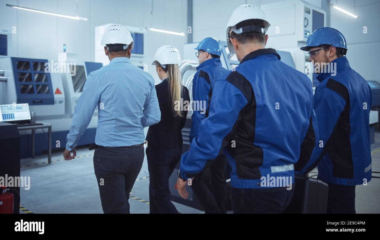 Capo di progetto femminile, team di ingegneri, lavoratori, sicurezza, Ispettore di controllo indossare i cappelli duri camminare attraverso la fabbrica industriale. Struttura con Foto Stock