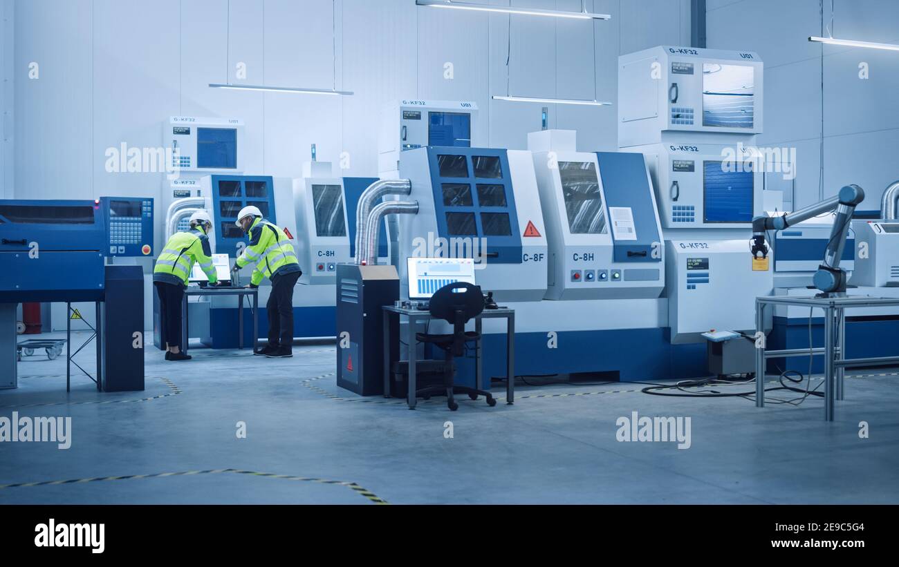 Capo ingegnere e Project Manager indossare giubbotti di sicurezza e cappelli duri lavorare su computer, parlare, ottimizzare la linea di produzione. In primo piano: Industria 4.0 Foto Stock