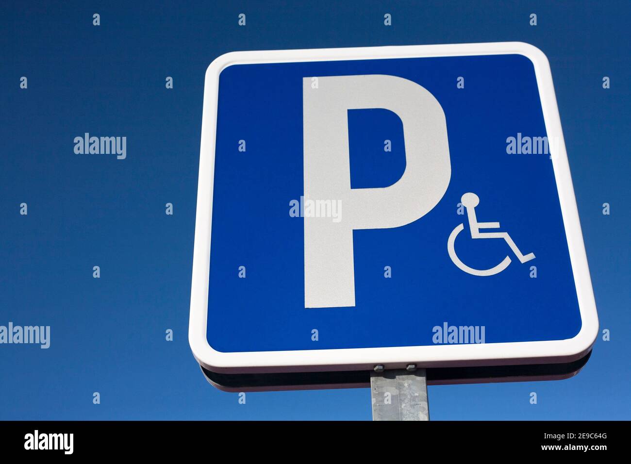 Segnale che indica il parcheggio prioritario per i veicoli con disabilità. Sfondo blu cielo. Foto Stock