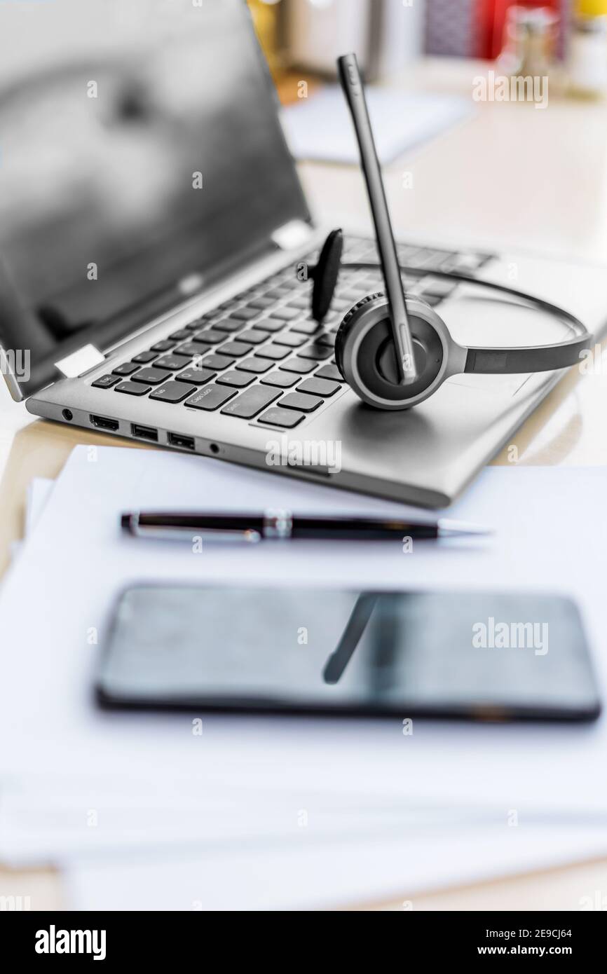 Computer portatile e telefono. Schermo mockup, carte, penna e cuffie sul tavolo. Helpdesk o cuffia per call center. Apprendimento a distanza o lavoro da casa, corsi online o concetto di centro di supporto. Foto Stock