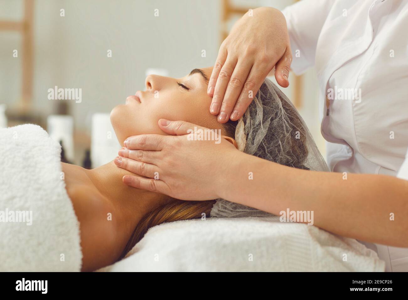Primo piano di una massaggiatrice professionista che fa un massaggio viso e testa per la sua cliente femminile. Foto Stock