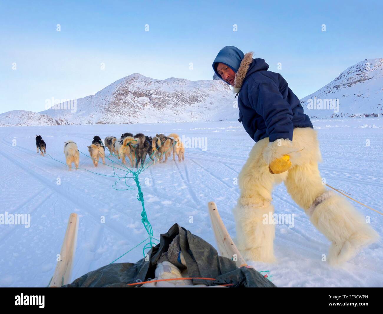 Saltando sulla slitta. Cacciatore inuit con pantaloni e stivali tradizionali realizzati in pelliccia di orso polare sul ghiaccio marino della Baia di Melville vicino a Kullorsuaq Foto Stock