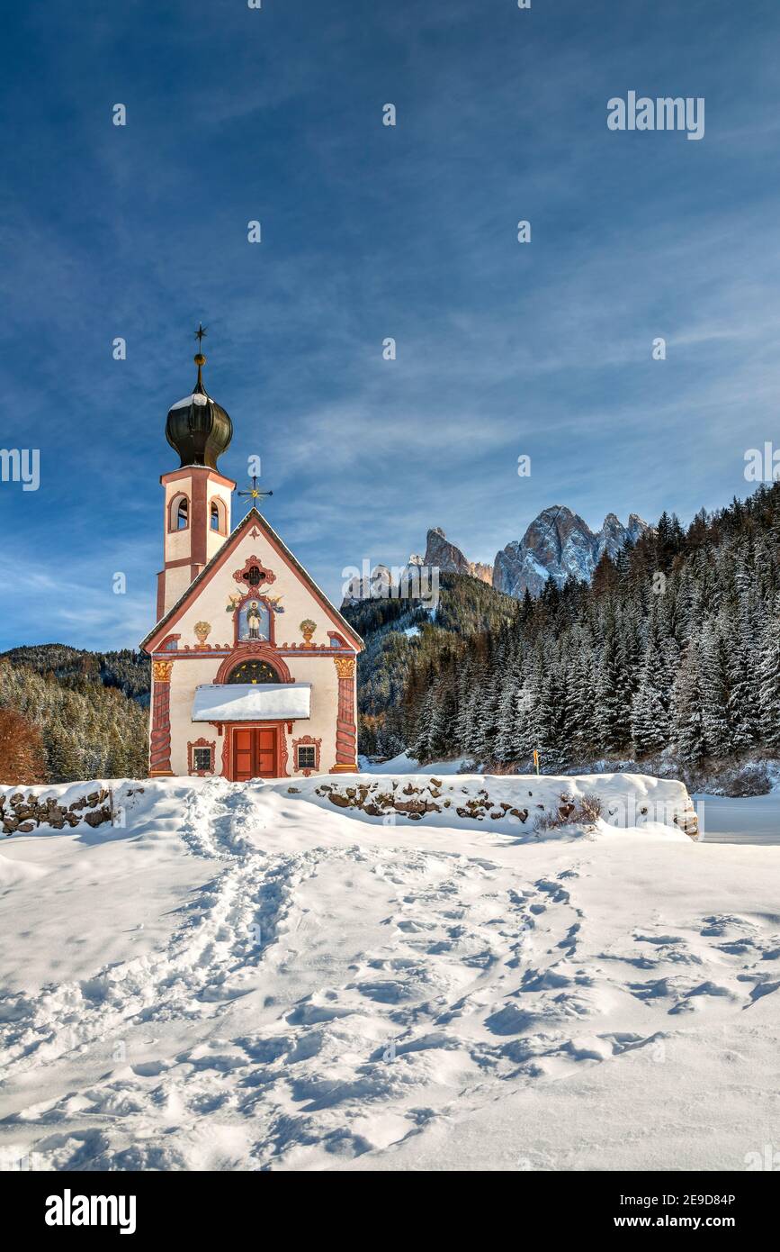 Vista panoramica invernale sulla chiesa di St Johann in Ranui con le Dolomiti di Odle alle spalle, Val di Funes, Alto Adige, Italia Foto Stock