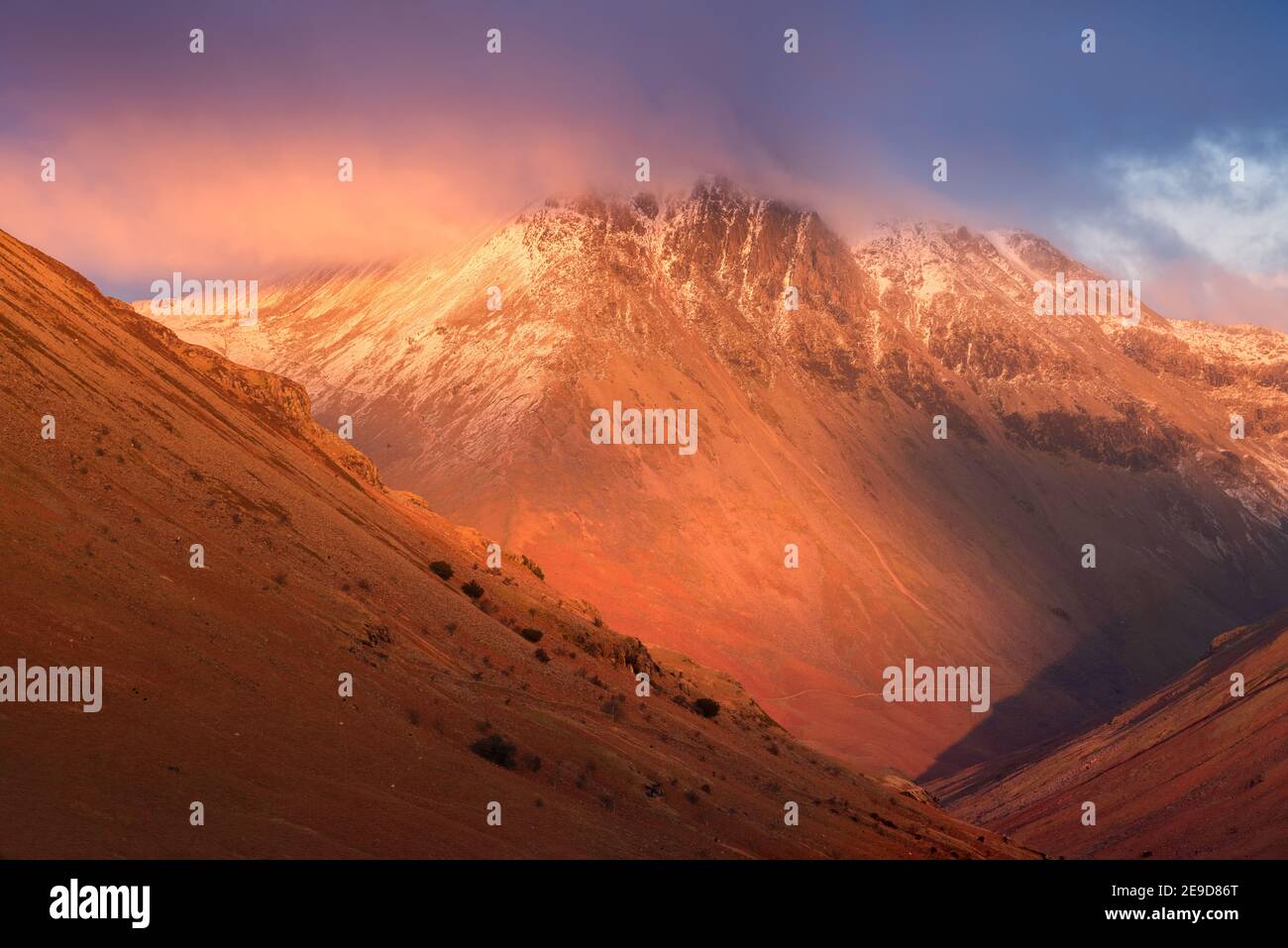 Maestose montagne innevate con nuvole scure e suggestive e luce rossa invernale. Natura sfondo. Lake District National Park, Regno Unito. Foto Stock