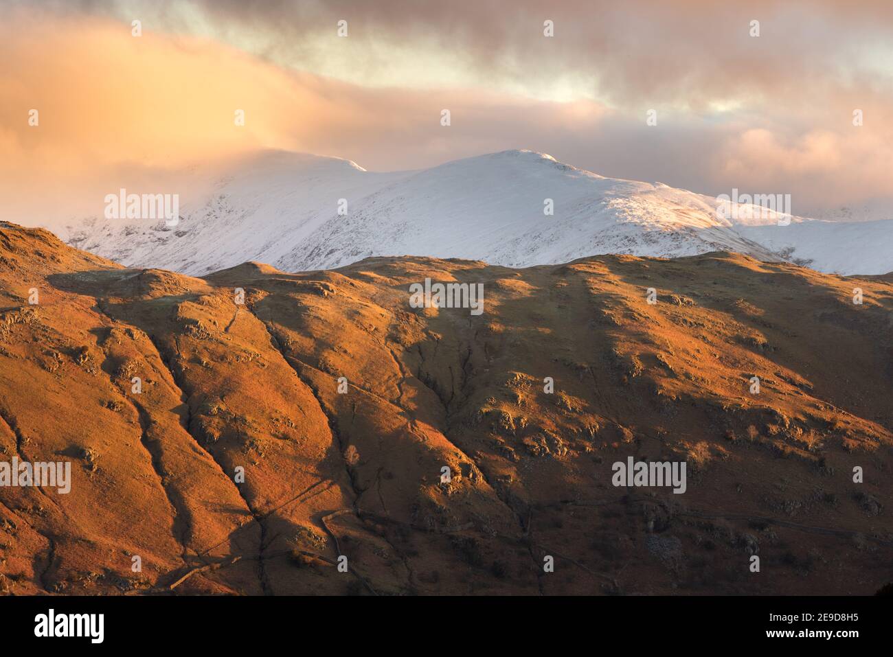 Lake District catena montuosa coperta di neve all'alba con bella luce dorata sulle campane. Foto Stock