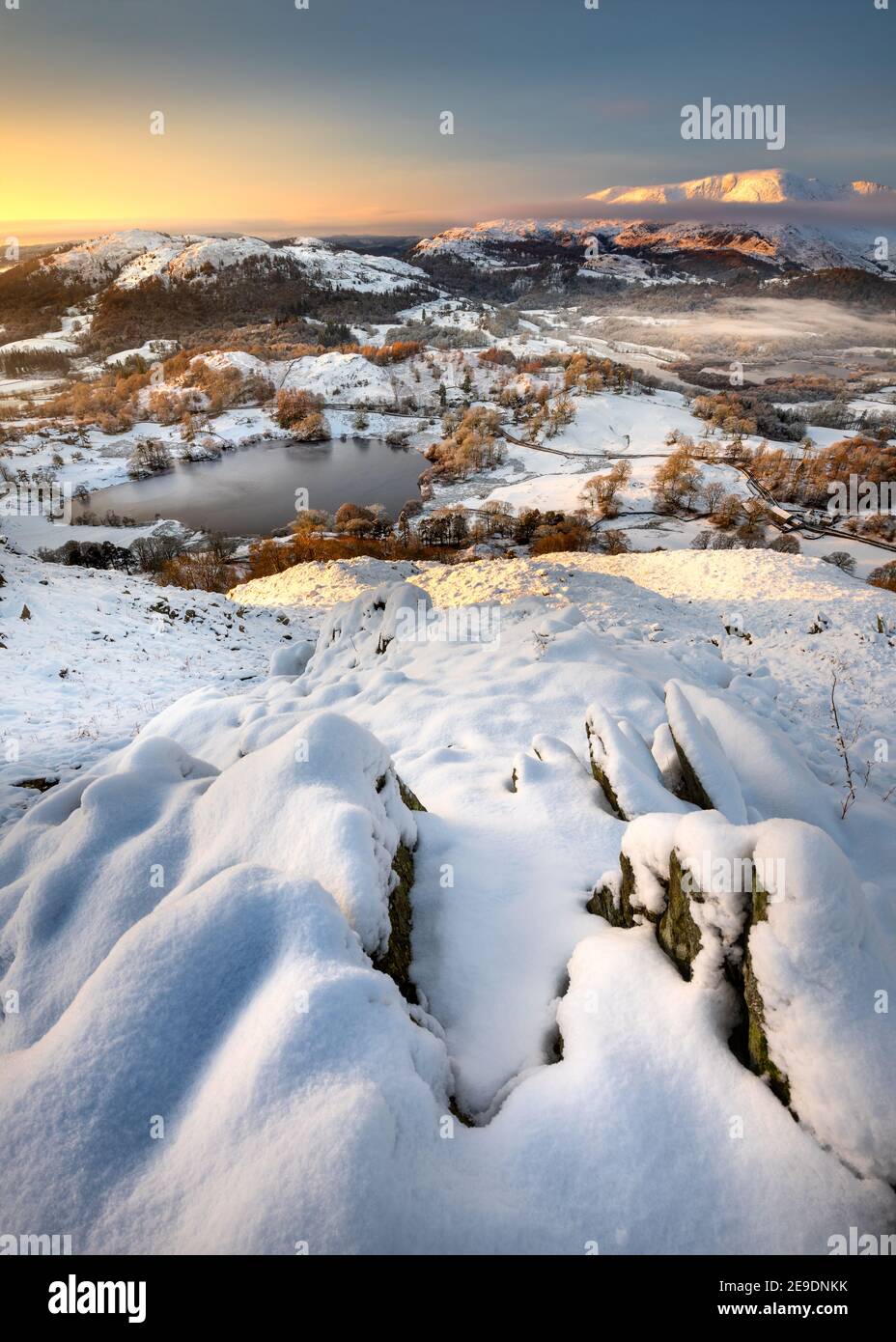 Neve sulle montagne sopra Loughrigg Tarn in una fredda mattina d'inverno con bella luce dorata. Panorama mozzafiato della campagna inglese. Lake District, Regno Unito Foto Stock