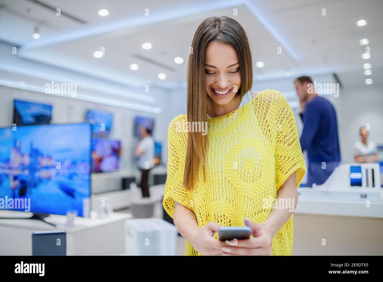 Felice giovane donna in cerca di smartphone da acquistare. Smartphone a mani libere. Foto Stock