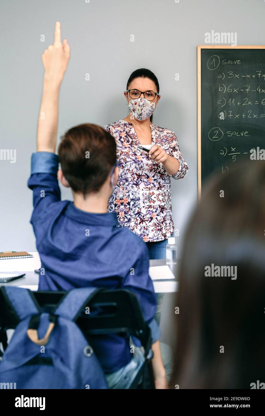 Insegnante con maschera in classe matematica con studente che alza la mano Foto Stock