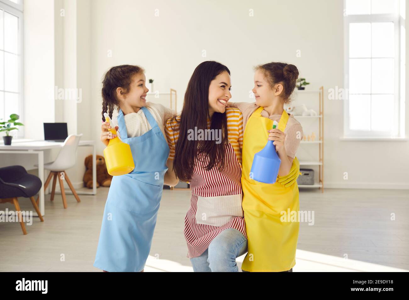 Felice madre sorridente abbraccia le sue due piccole figlie gemelle che la aiutarono a pulire la casa. Foto Stock