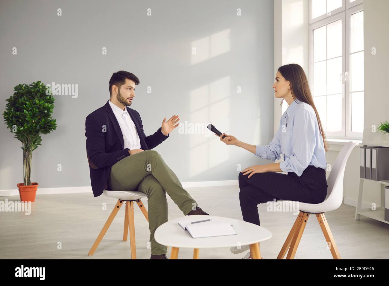 Donna con un microfono in mano si siede davanti a un uomo famoso e lo intervista. Foto Stock