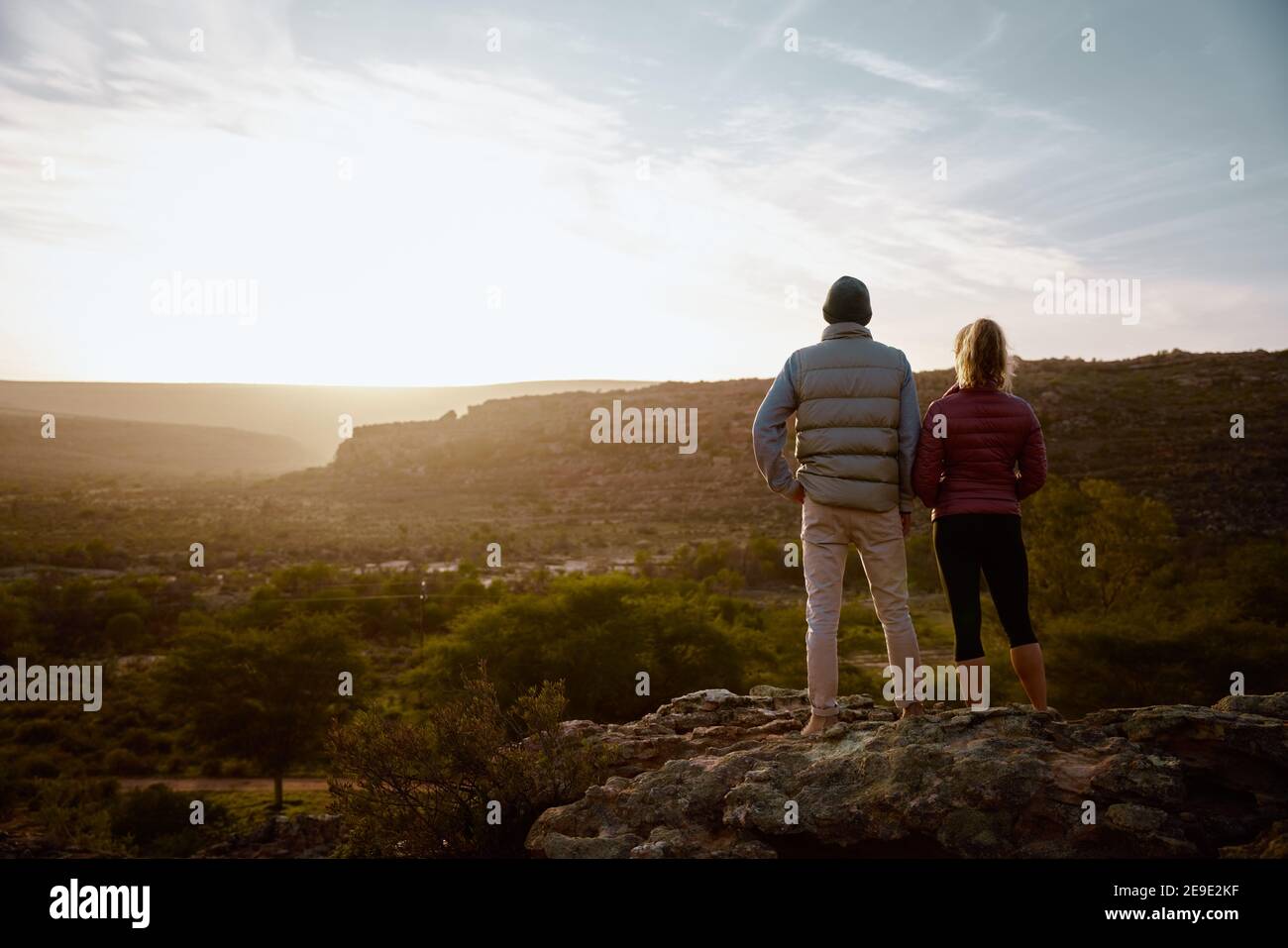 Vista posteriore del giovane uomo e della donna in piedi in montagna scogliera che guarda all'alba Foto Stock