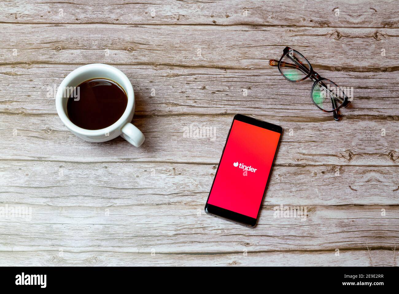 Un telefono cellulare o un telefono cellulare posto su un tavolo O scrivania con l'app di datazione Tinder aperta e una caffè accanto ad esso Foto Stock