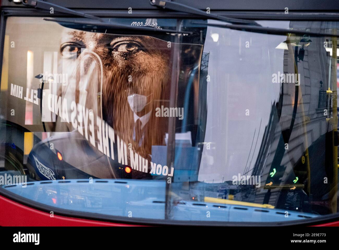 Visto riflesso nel parabrezza di un autobus di passaggio, un annuncio del governo NHS (National Heath Service) mostra il volto di un paziente di Covid, esortando i londinesi a rimanere a casa e a non correre rischi o piegare le regole durante il terzo blocco della pandemia di Coronavirus, A Piccadilly Circus nel West End della capitale, il 3 febbraio 2021, a Londra, Inghilterra. Foto Stock