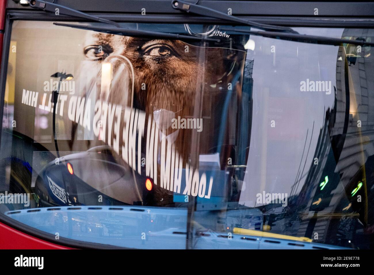 Visto riflesso nel parabrezza di un autobus di passaggio, un annuncio del governo NHS (National Heath Service) mostra il volto di un paziente di Covid, esortando i londinesi a rimanere a casa e a non correre rischi o piegare le regole durante il terzo blocco della pandemia di Coronavirus, A Piccadilly Circus nel West End della capitale, il 3 febbraio 2021, a Londra, Inghilterra. Foto Stock