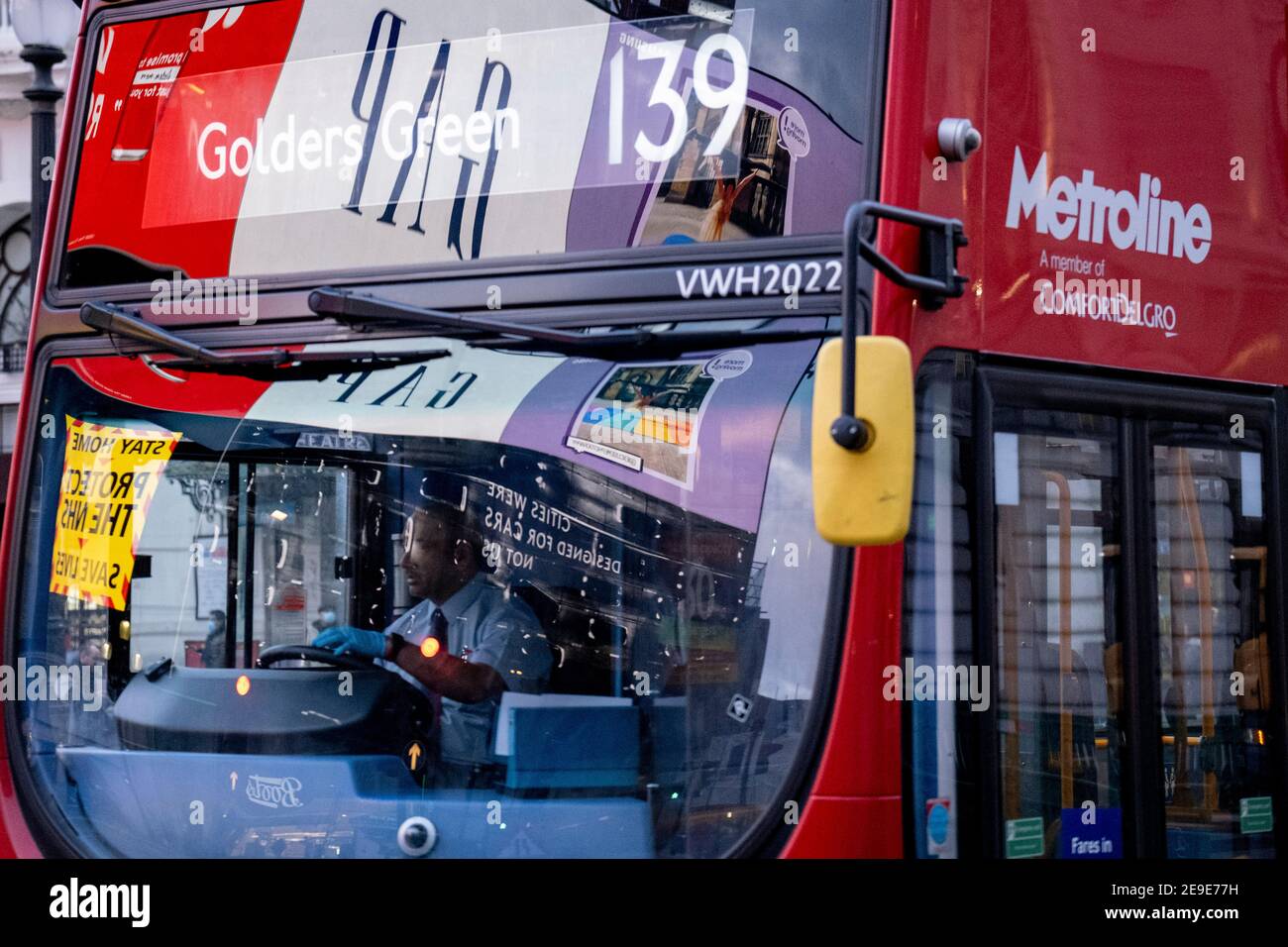 Visto riflesso nel parabrezza di un autobus di passaggio, un annuncio del governo NHS (National Heath Service) mostra il volto di un paziente di Covid, esortando i londinesi a rimanere a casa e a non correre rischi o piegare le regole durante il terzo blocco della pandemia di Coronavirus, A Piccadilly Circus nel West End della capitale, il 3 febbraio 2021, a Londra, Inghilterra. Foto Stock