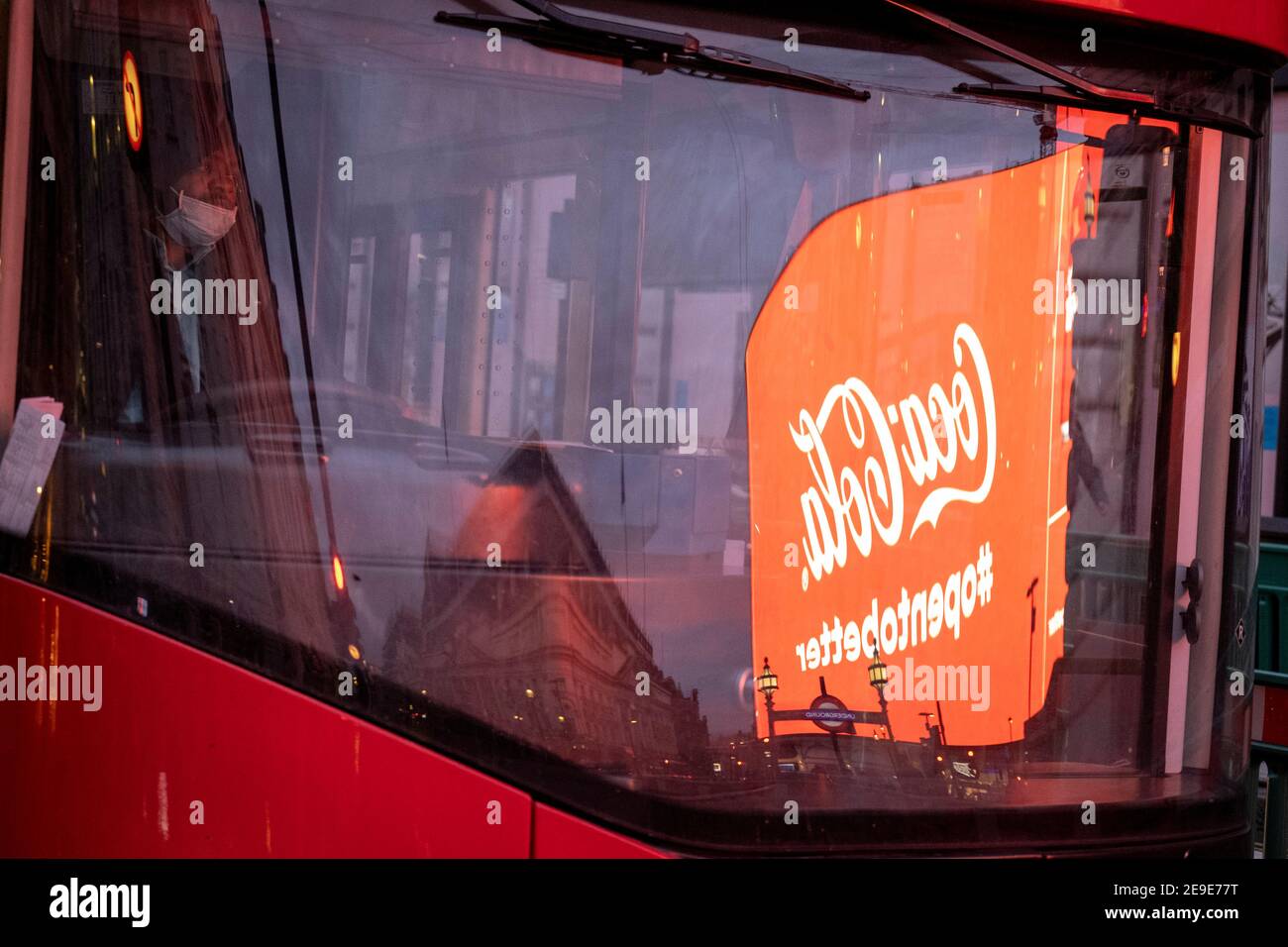 Visto riflesso nel parabrezza di un autobus di passaggio, un annuncio Coca-Cola si riflette accanto al pilota di Piccadilly Circus nel West End della capitale, il 3 febbraio 2021, a Londra, Inghilterra. Foto Stock