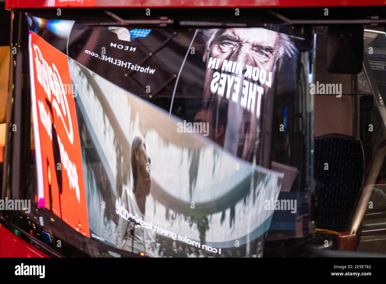 Visto riflesso nel parabrezza di un autobus di passaggio, un annuncio del governo NHS (National Heath Service) mostra il volto di un paziente di Covid, esortando i londinesi a rimanere a casa e a non correre rischi o piegare le regole durante il terzo blocco della pandemia di Coronavirus, A Piccadilly Circus nel West End della capitale, il 2 febbraio 2021, a Londra, Inghilterra. Foto Stock