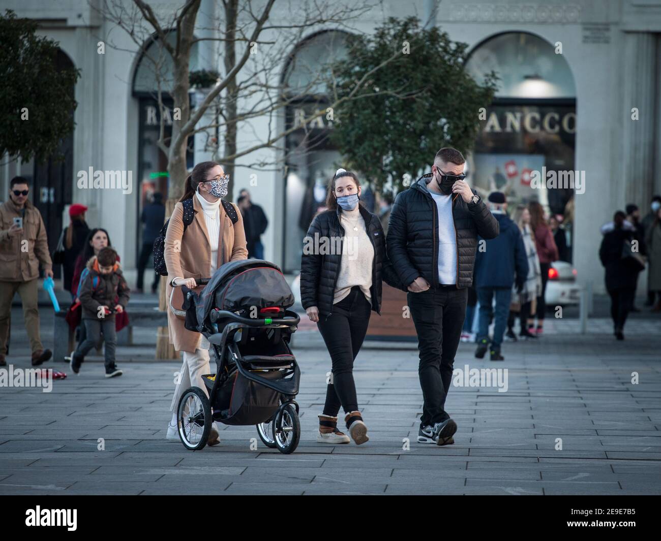 BELGRADO, SERBIA - 1 GENNAIO 2021: Famiglia europea, padre e madre, e il loro bambino, in passeggino, a piedi indossare maschera di protezione equipem Foto Stock