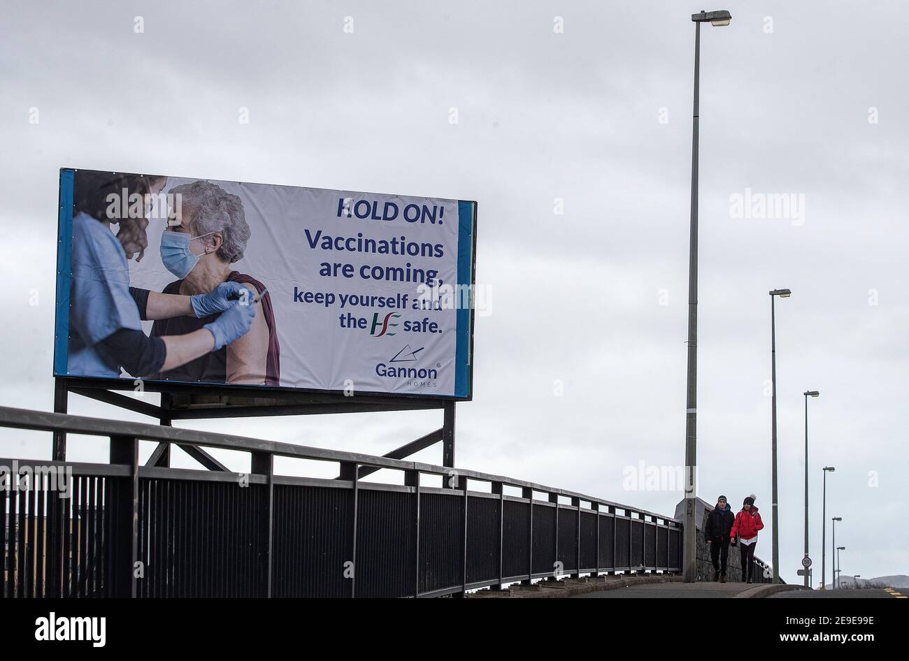 La gente passa davanti a un tabellone nella parte settentrionale di Dublino, Irlanda, esortando le persone a tenere e a preannunciarsi l'arrivo delle vaccinazioni come ministro della Salute Stephen Donnelly ha dichiarato oggi di aver firmato l'autorizzazione per l'uso del vaccino AstraZeneca. Data immagine: Giovedì 4 febbraio 2021. Foto Stock