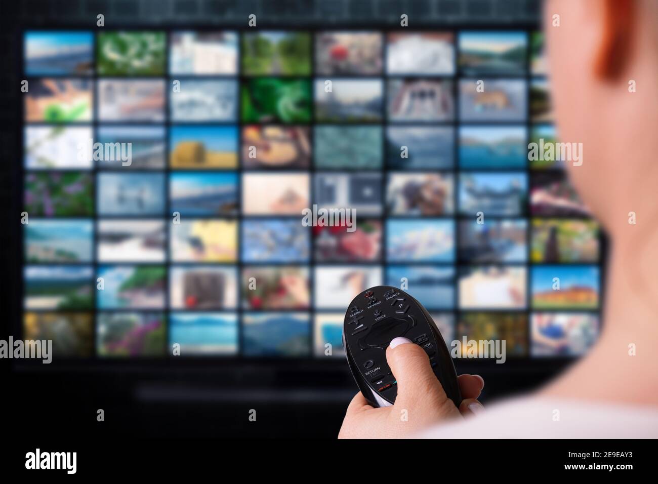 Donna tiene il servizio video del telecomando su richiesta sulla TV di sfondo con l'icona del fornitore VOD. Video online Media TV. Servizio video con streaming Internet Foto Stock