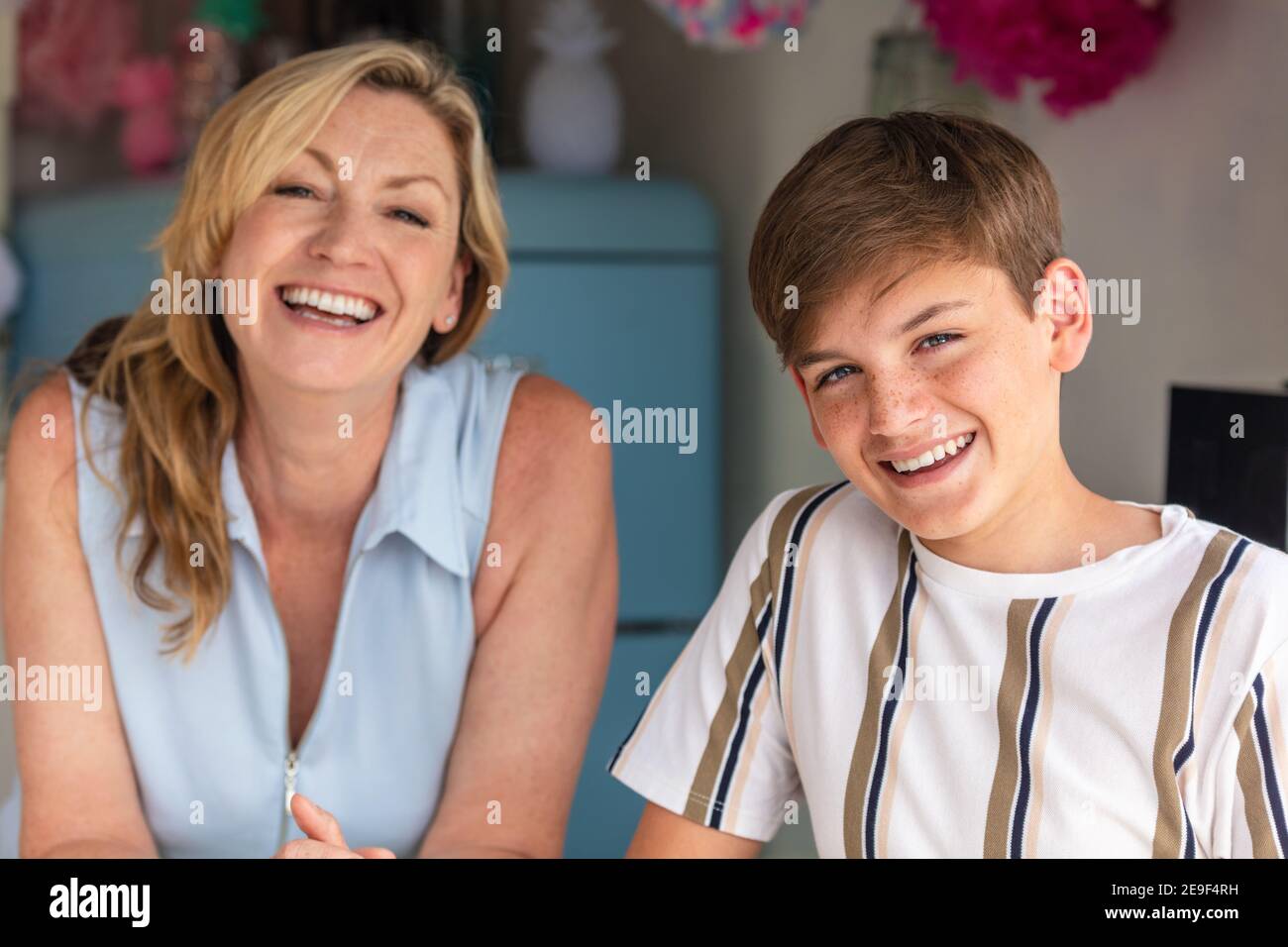 Figlio adolescente ridendo in una cucina con lui madre fuori fuoco dietro di lui Foto Stock