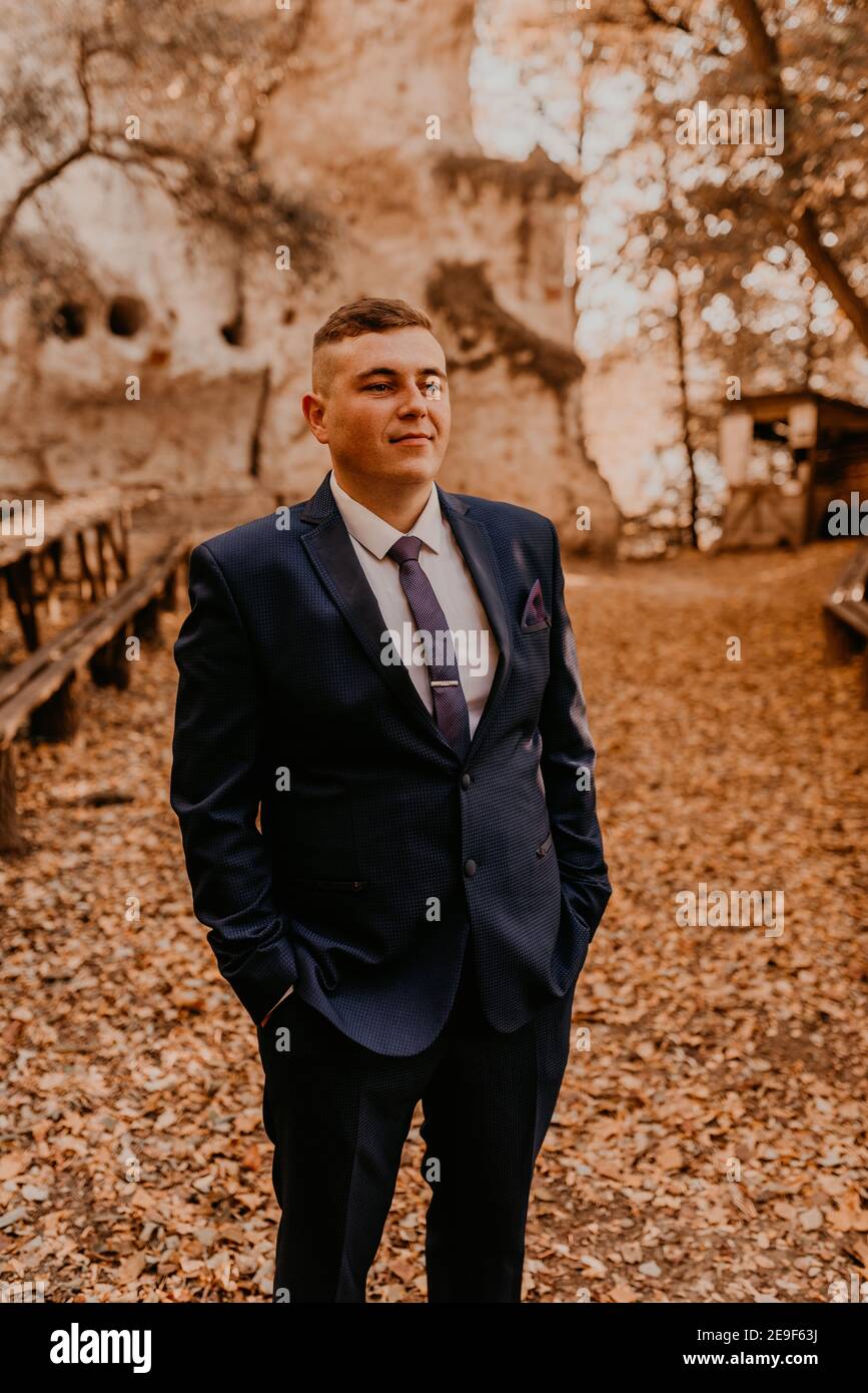 un uomo in tuta formale lo sposo si trova nella foresta autunnale che tiene le mani in tasca. monastero di roccia a bakota Foto Stock