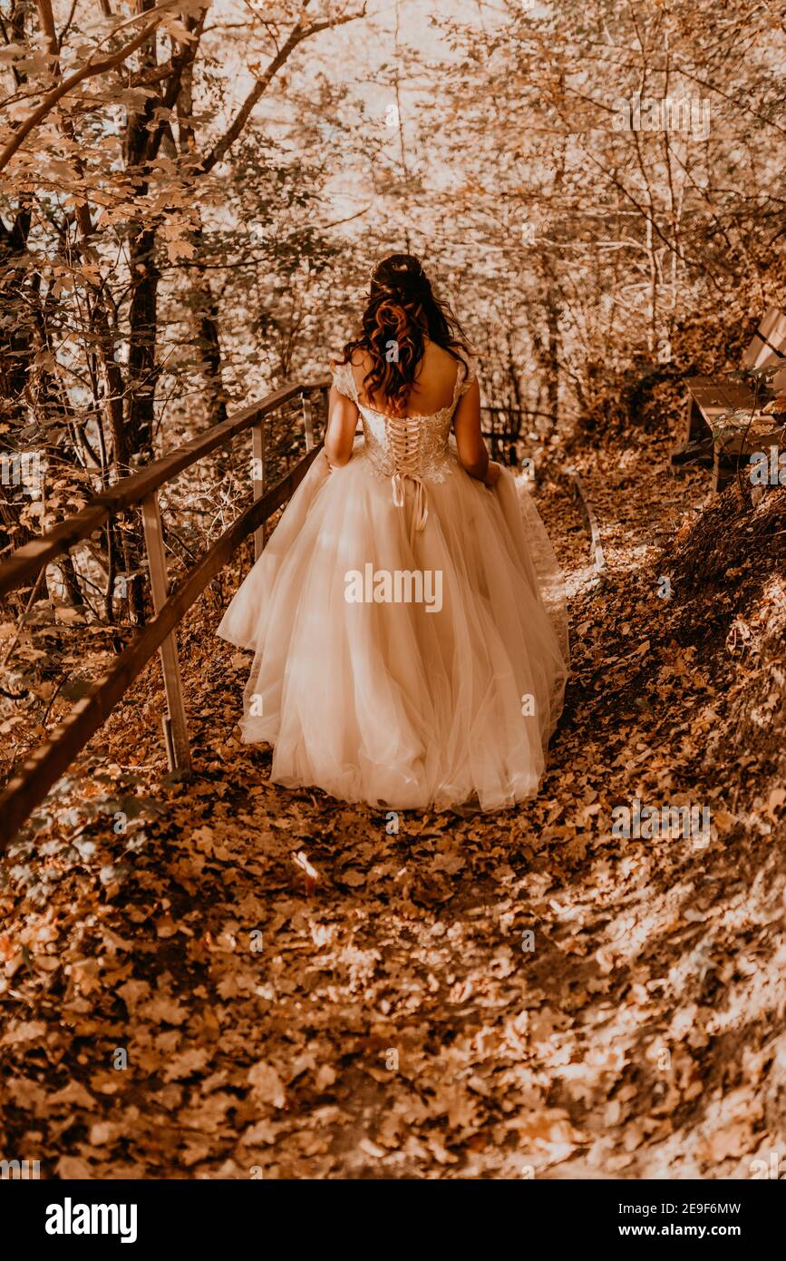 sposa donna in abito da sposa bianco con acconciatura trucco e. crown sulla sua testa cammina attraverso la foresta d'autunno su caduto foglie arancioni Foto Stock