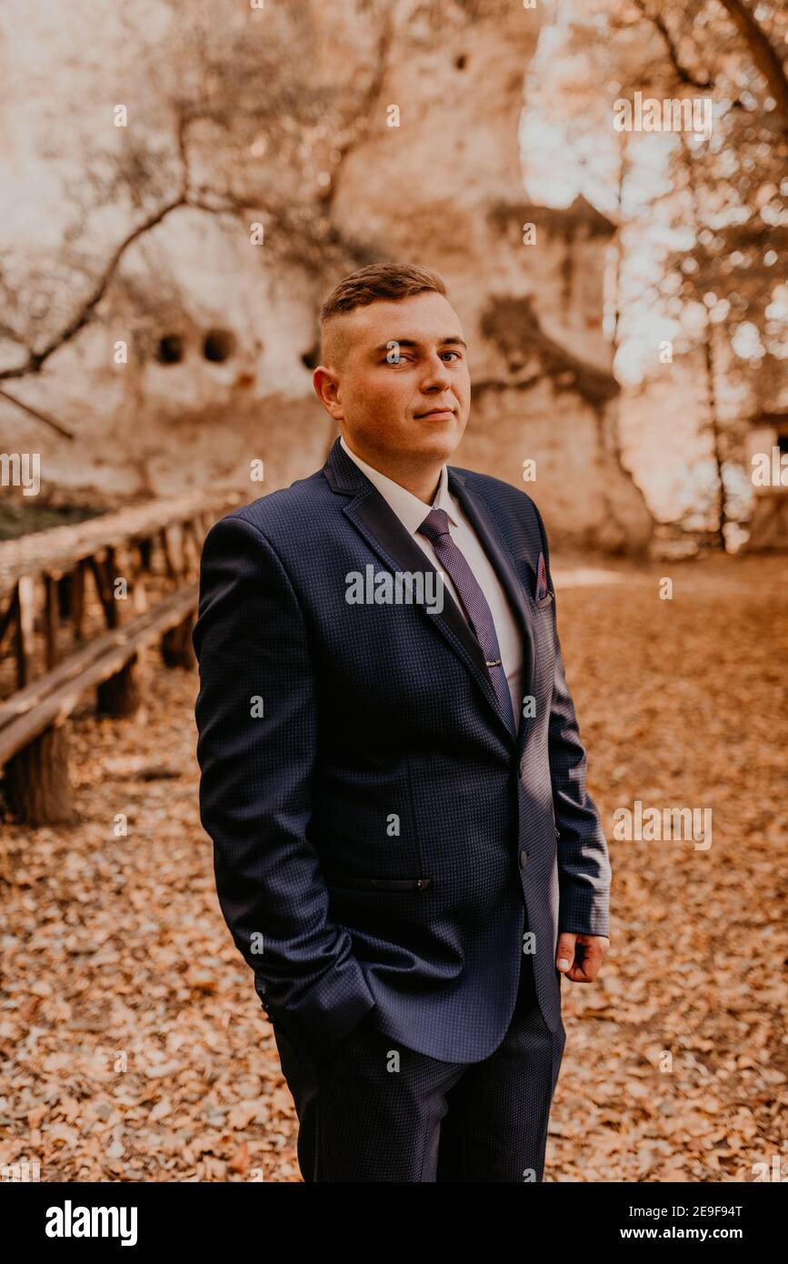 un uomo in tuta formale lo sposo si trova nella foresta autunnale che tiene le mani in tasca. monastero di roccia a bakota Foto Stock
