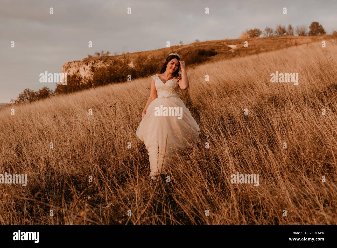 bella donna bruna sposa in abito bianco e vestito sono camminando su erba alta in campo in estate Foto Stock