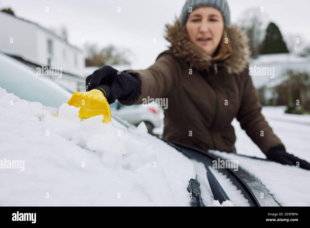Donna in inverno Clearing neve dal parabrezza di auto con Raschiatore Foto Stock