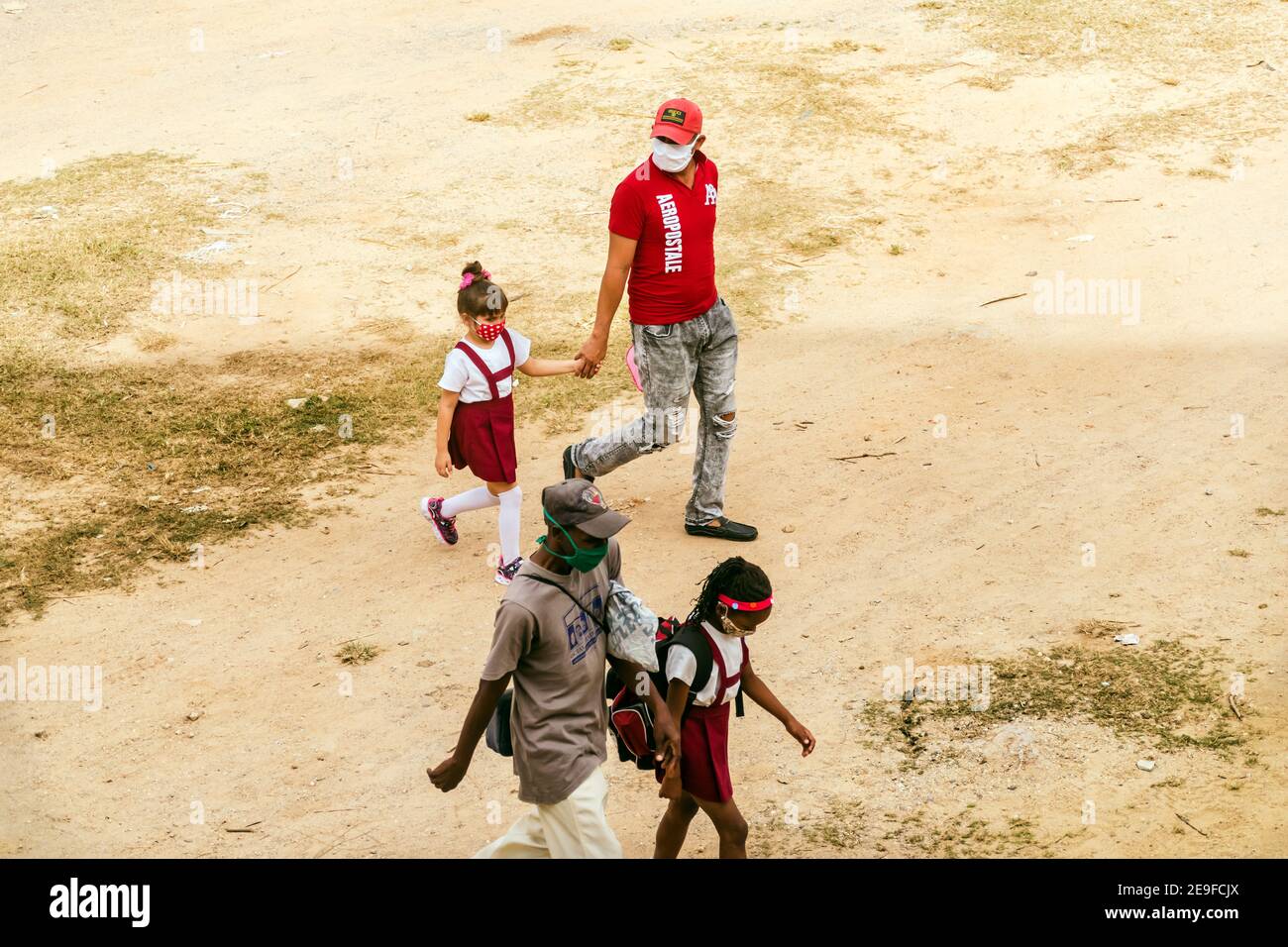 Genitori maschi che camminano le loro figlie alla scuola elementare di Cuba, ciascuno sta tenendo la sua figlia´s mano. Razze etniche diverse Foto Stock
