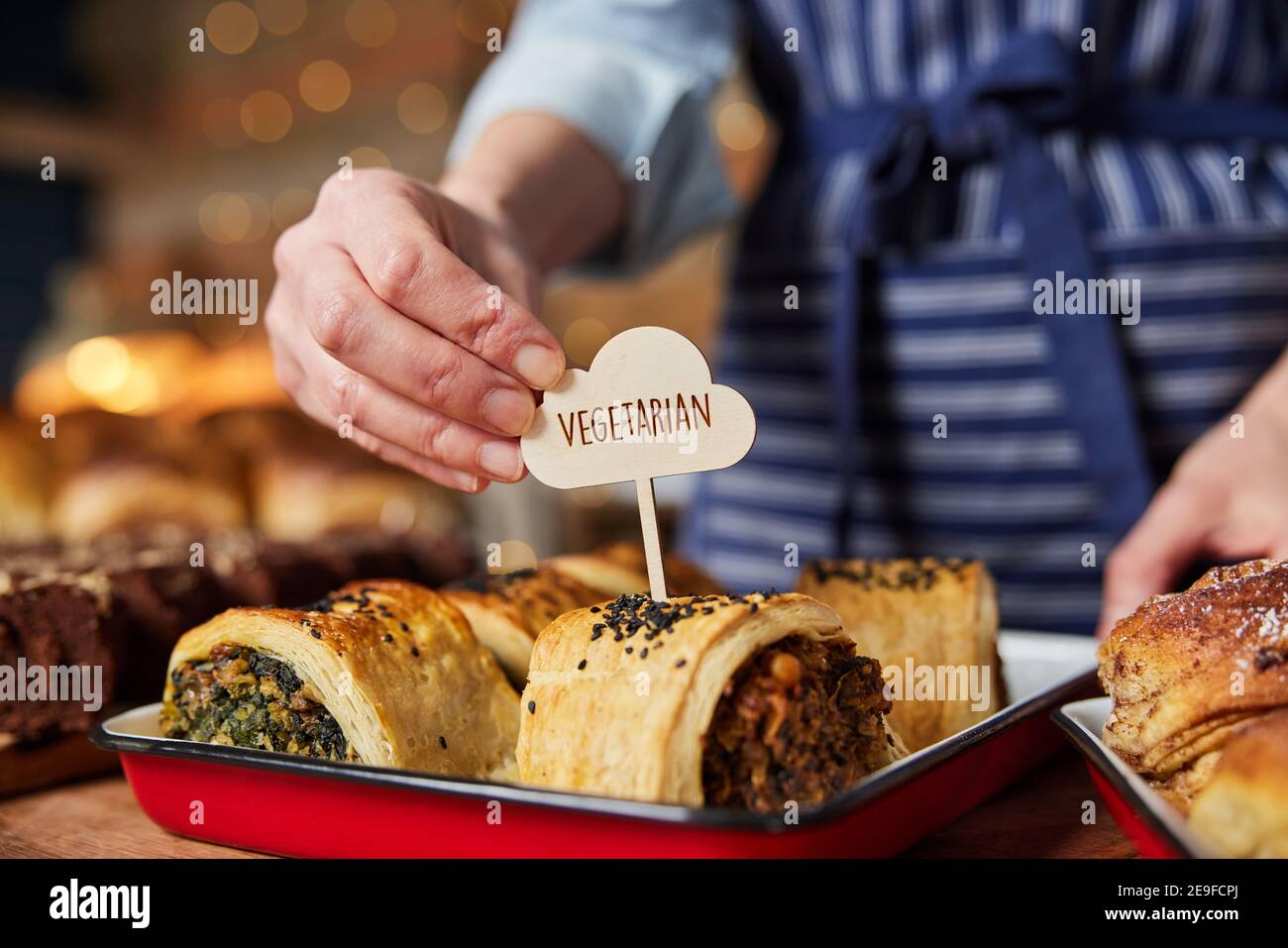 Assistente vendite in panetteria che mette Vegetarian Free Label in fresco Rotolo di salato al forno Foto Stock