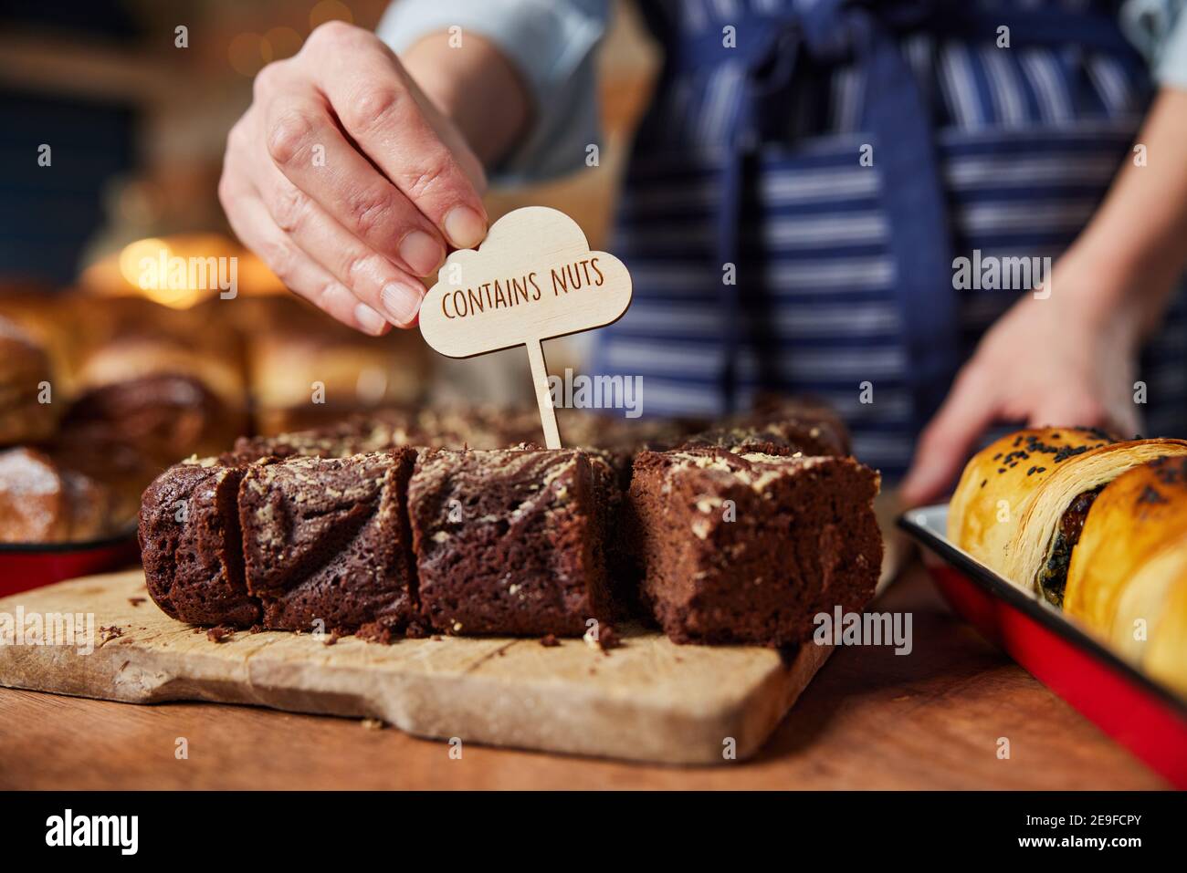 Sales Assistant in panetteria che mette contiene l'etichetta NUTS nella pila Di brownie appena sfornate Foto Stock