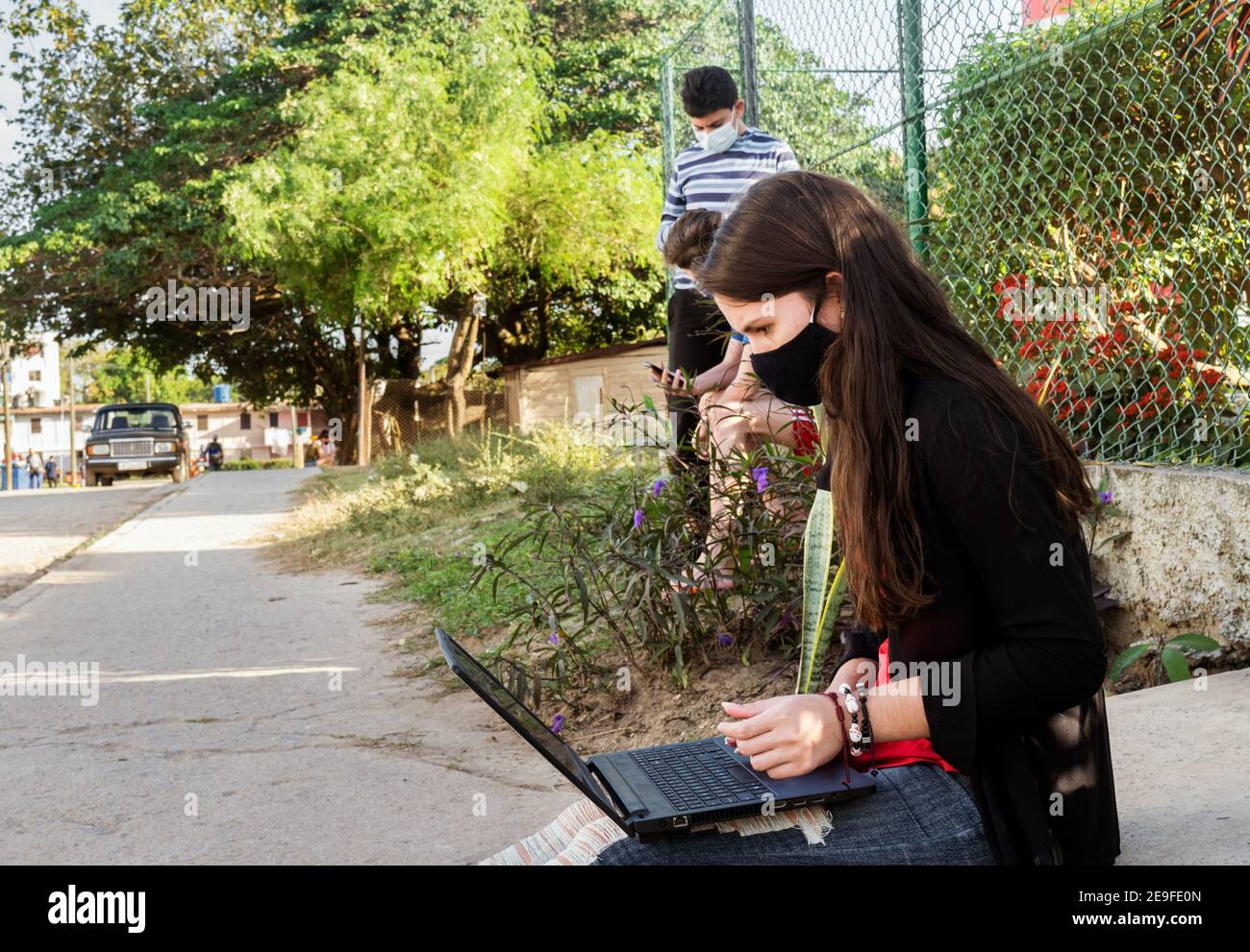 Giovani cubani con il loro computer portatile e telefoni cellulari all'aperto vicino La ricezione di un'antenna Wi-Fi che tenta di accedere a Internet connessione Foto Stock