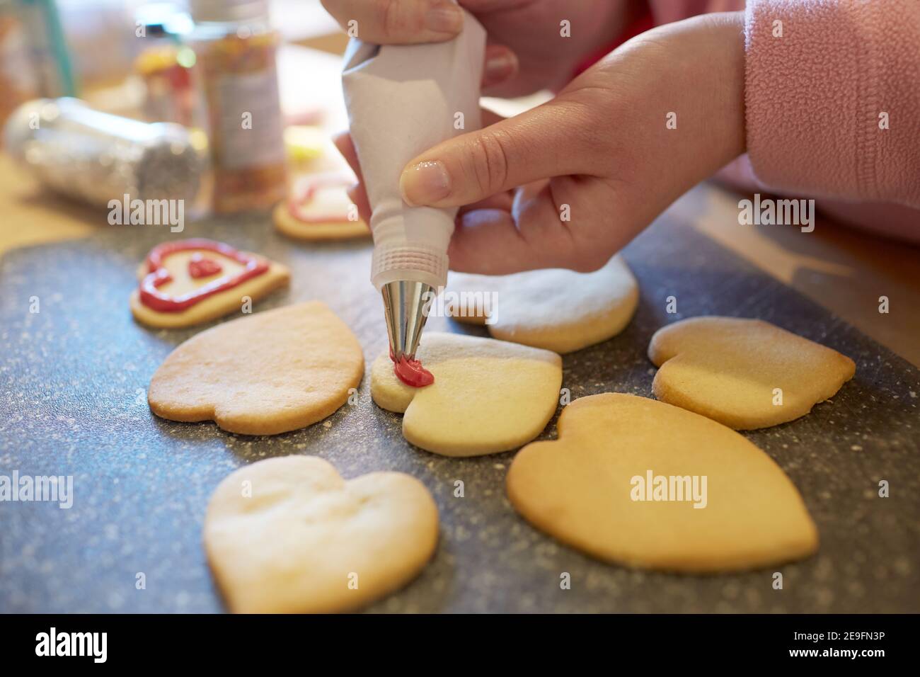 Una fotografia ravvicinata di una donna che decora i biscotti fatti in casa a forma di cuore. Foto Stock