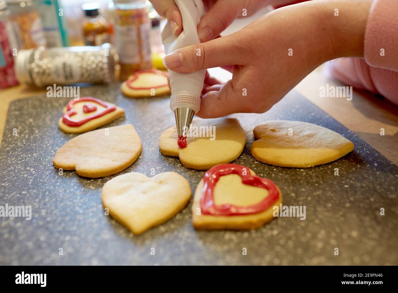 Una fotografia ravvicinata di una donna che decora i biscotti fatti in casa a forma di cuore. Foto Stock