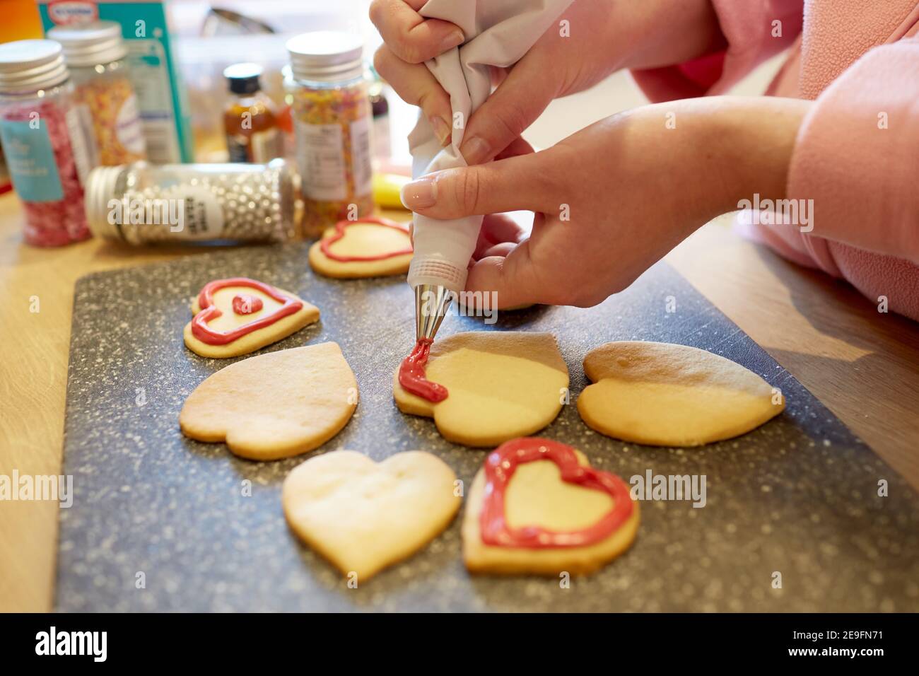 Una fotografia ravvicinata di una donna che decora i biscotti fatti in casa a forma di cuore. Foto Stock