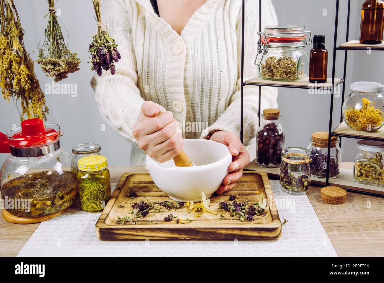 Primo piano vista di erborista donna mescolando varie erbe secche per il tè medicinale tradizionale con mortaio e pestello. Erbe secche in vasi di vetro. Foto Stock