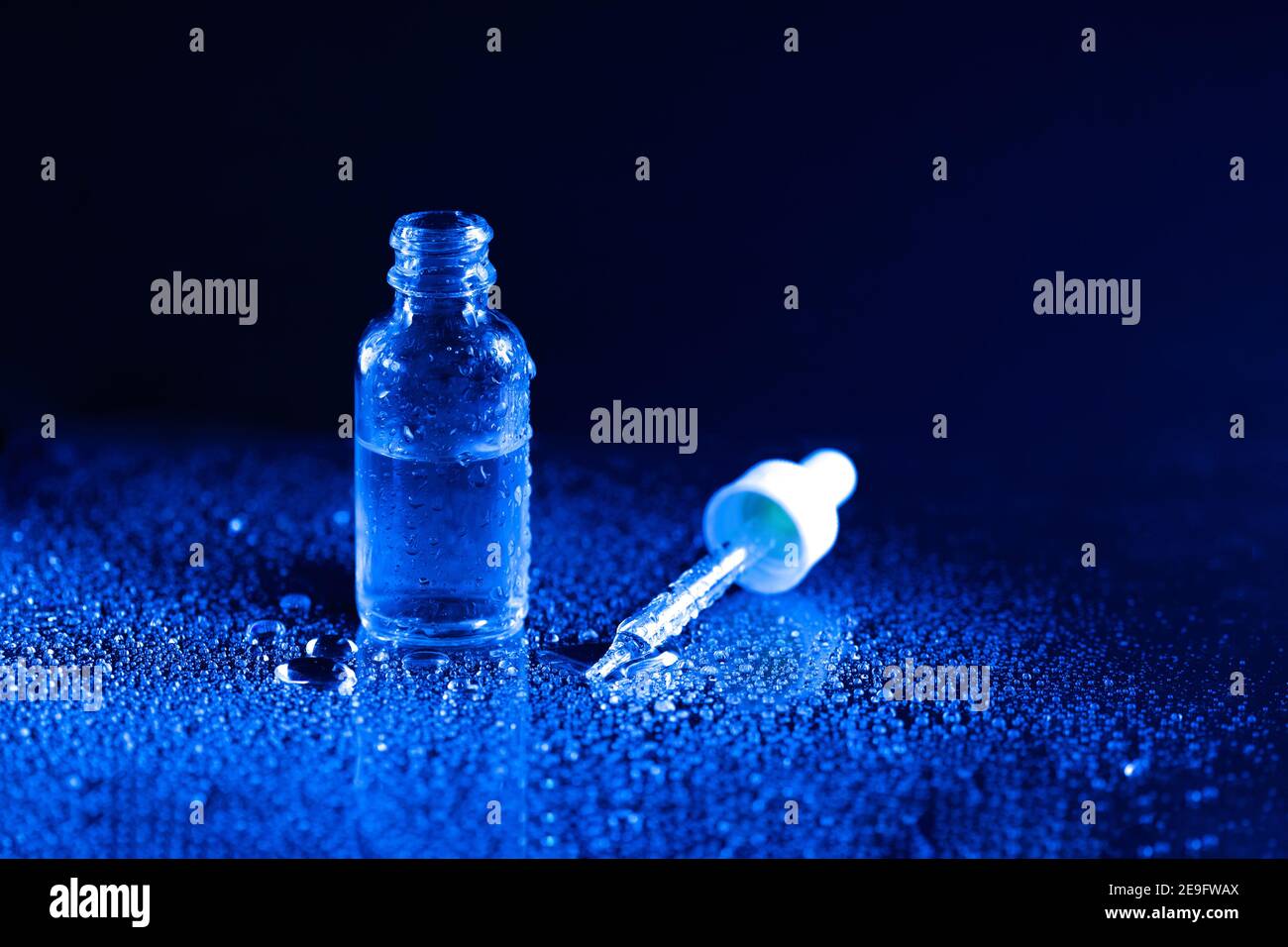 Flacone per tintura in vetro con contagocce su fondo nero e blu con gocce di liquido e schizzi sulla superficie riflettente. Test di laboratorio medico. IO Foto Stock