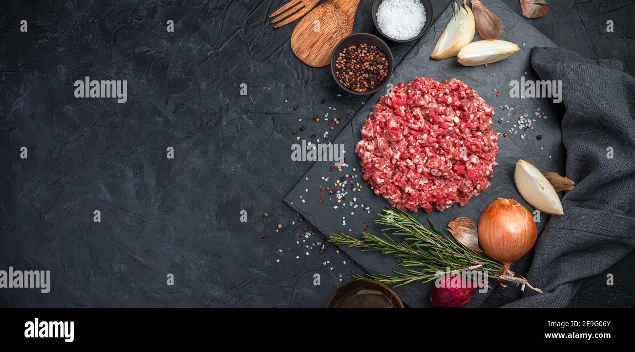 Macinare la carne di tacchino con pepe, cipolla e rosmarino su fondo nero di cemento. Foto Stock