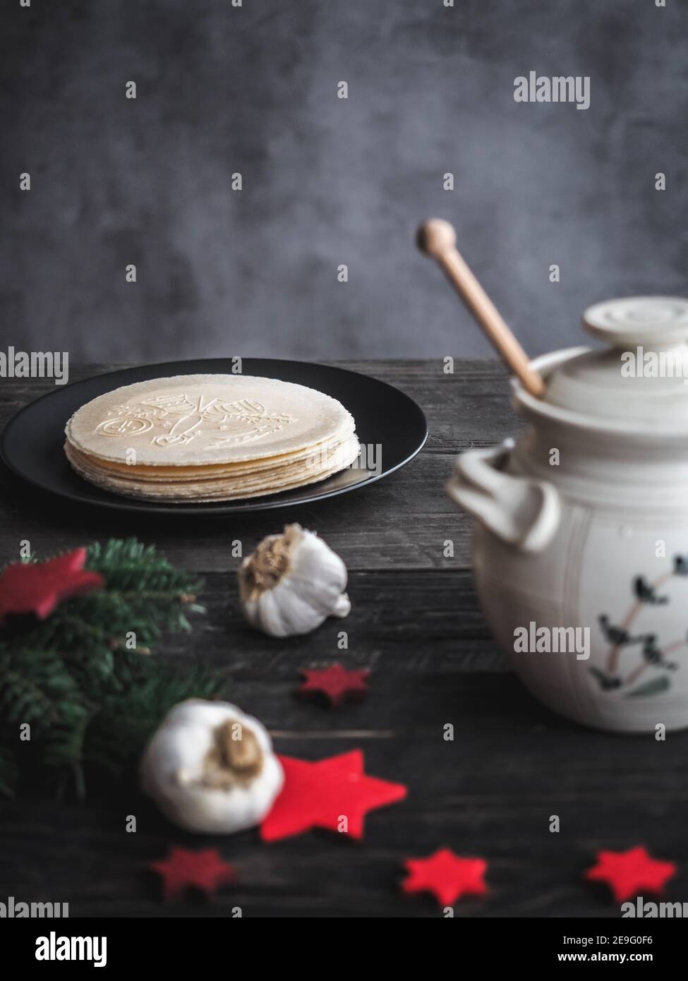 Wafer della vigilia di Natale con pentola di miele e bulbi di aglio su tavolo di legno. Buio e moody. Spazio di copia. Foto Stock