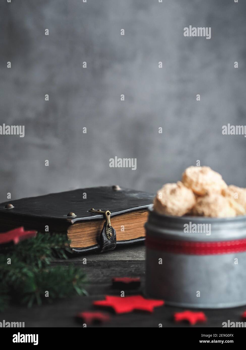 Biscotti meringa di cocco di Natale in scatola di metallo e vecchia bibbia sullo sfondo. Buio e moody. Spazio di copia. Foto Stock