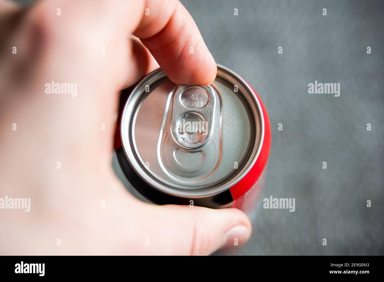 Tirare la linguetta di una lattina di bevande con una mano maschio sinistra. Apertura di una bevanda rinfrescante come cola o energydrink dopo una dura giornata Foto Stock