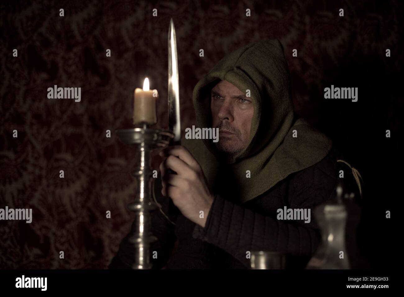 Il personaggio medievale con cappuccio si siede minacciosamente a lume di candela con pugnale Foto Stock