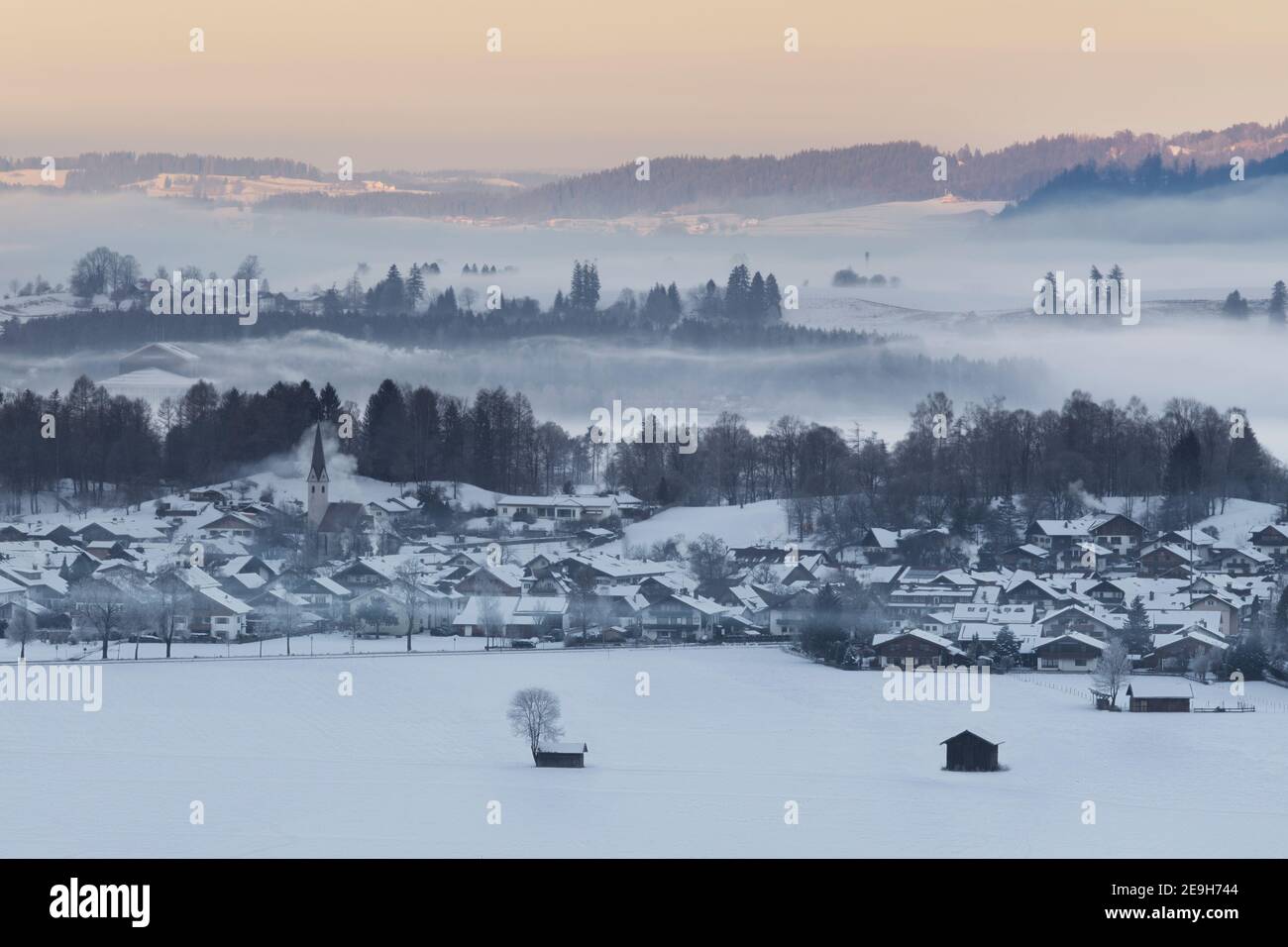 Alba invernale sul villaggio di Schwangau con montagne e foreste foggose Foto Stock